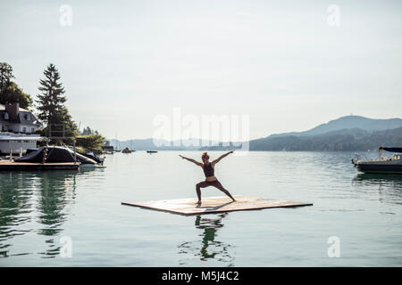 La donna a praticare yoga su zattera in un lago Foto Stock