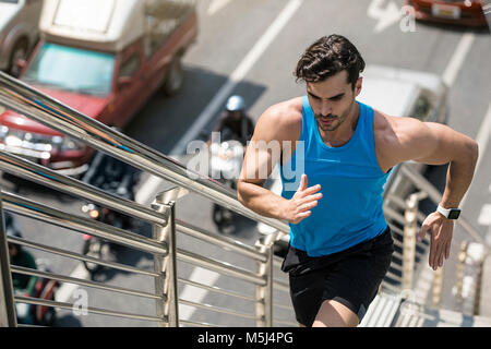 Uomo in blu maglietta fitness in esecuzione al piano di sopra in città Foto Stock