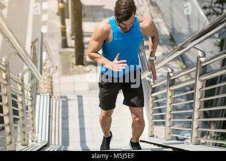 Uomo in blu maglietta fitness in esecuzione al piano di sopra in città Foto Stock