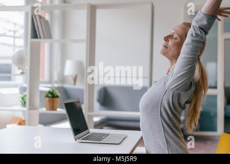 Donna con notebook alla scrivania in ufficio stretching Foto Stock