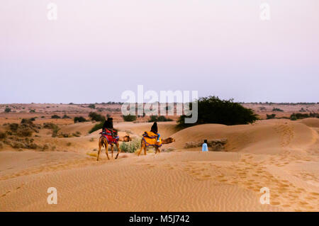 Bikaner, India - 29 DIC 2017: Camel proprietario tenendo un cammello verso il tramonto in lontananza sulla sabbia soffice del Thar Foto Stock