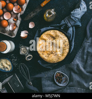 Uova strapazzate o frittata in ghisa padella e accessori da cucina vista dall'alto. Uova,guscio,latte,formaggio parmigiano,profumato Rosmarino sale,l'olio d'oliva,p Foto Stock