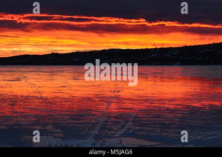 Una mattina presto, winter sunrise, riflette il lago ghiacciato con meravigliose arancione, blu, rosa e rossastre nubi all'orizzonte Foto Stock