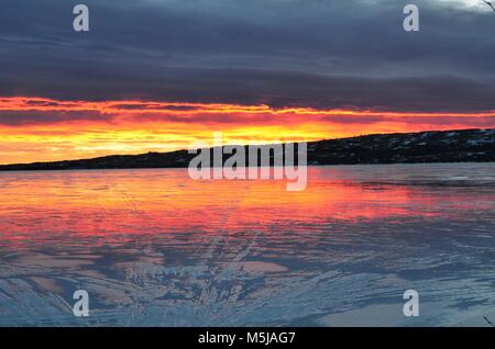 Una mattina presto, winter sunrise, riflette il lago ghiacciato con meravigliose arancione, blu, rosa e rossastre nubi all'orizzonte Foto Stock