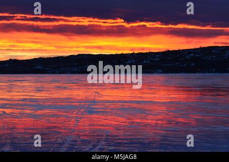 Una mattina presto, winter sunrise, riflette il lago ghiacciato con meravigliose arancione, blu, rosa e rossastre nubi all'orizzonte Foto Stock