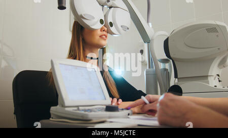 Bionda giovane femmina facendo prova di occhio con all'ottico optometrista nel centro medico Foto Stock