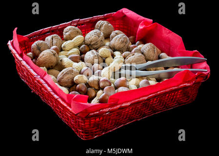 Red cesto in vimini con frutta secca, nocciola, noci, mandorle, arachidi e uno schiaccianoci su sfondo nero Foto Stock