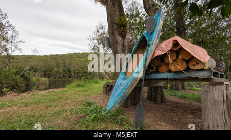 Un kayak e di legna da ardere impilati su una proprietà accanto a Warrell Creek che unisce il fiume Nambucca sulla costa nord del NSW, Australia Foto Stock