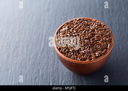 Narural materie semi di lino in una argilla ceramica ciotola isolato su sfondo scuro, close-up. Utile e semi oleosi nutrizionale per le attività quotidiane di cottura. Eati sani Foto Stock