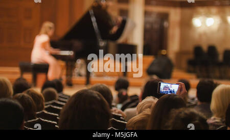 Gli spettatori in sala da concerto durante l esecuzione di pianoforte ragazza- persone prestazioni di scatto sullo smartphone Foto Stock