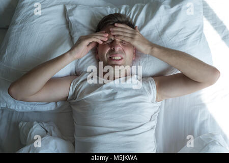 Uomo disteso nel letto di casa che soffrono di mal di testa o i postumi della sbornia Foto Stock