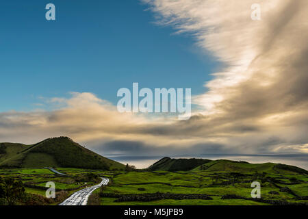 La strada attraverso il verde paesaggio collinare,cielo nuvoloso,isola di Pico,Azzorre,Portogallo Foto Stock