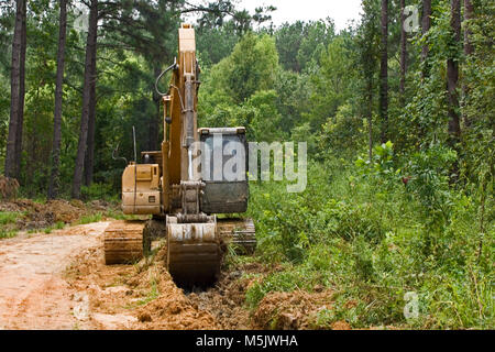 Cat 3200 trackhoe (via zappa, escavatore meccanico a pala) lo scavo di una fossa di scolo lungo una registrazione di ghiaia strada in Alabama River palude, in banner Foto Stock