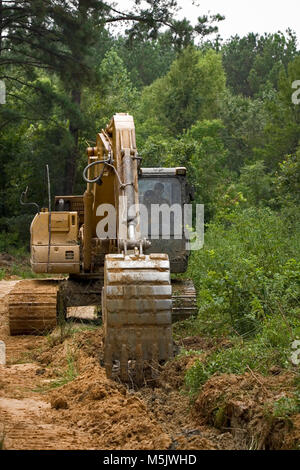 Cat 3200 trackhoe (via zappa, escavatore meccanico a pala) lo scavo di una fossa di scolo lungo una registrazione di ghiaia strada in Alabama River palude, in banner Foto Stock