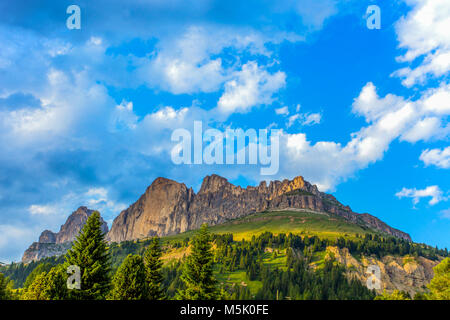 Vista sulle montagne del gruppo del Catinaccio (Rosengarten) con prati e abeti, sotto un azzurro cielo nuvoloso, Dolomiti, Italia Foto Stock