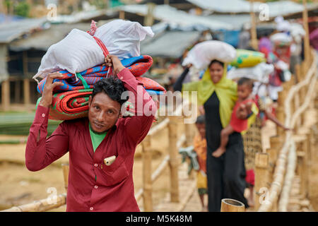 Trasporto ricovero di emergenza materiali e cibo, rifugiati Rohingya attraversare a piedi traballanti bridge nella tentacolare Kutupalong Refugee Camp in Bangladesh. Foto Stock