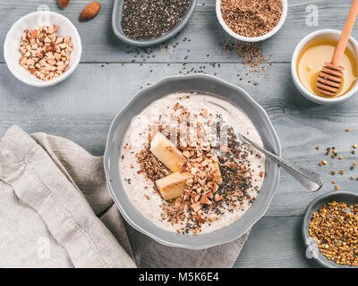 Per una notte di avena in un recipiente e ingredienti - banana, LSA, chia semi, mandorla, miele e polline in legno grigio sfondo tabella. Sana colazione fiocchi d'avena Foto Stock