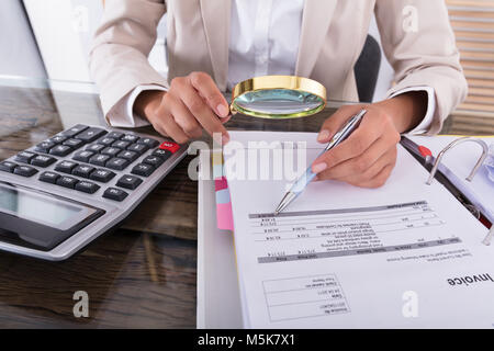 Close-up di giovane imprenditrice mano esaminando fattura con lente di ingrandimento sulla scrivania in ufficio Foto Stock