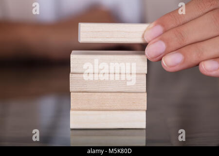 Close-up di imprenditrice mano posizionando il blocco di legno sulla torre di legno a tavola Foto Stock