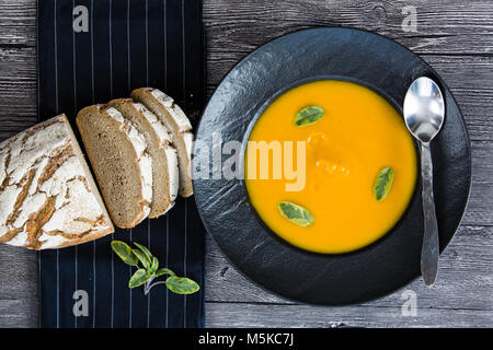 Zuppa di zucca in una piastra nera e pane rustico Foto Stock