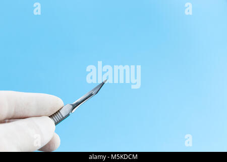 Un bisturi nelle mani dei medici in bianco guanti medicali isolato su sfondo blu spazio copia. Studio Shot Foto Stock