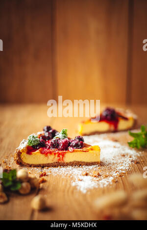 Bella italiana tradizionale cheesecake con frutti rossi, menta e zucchero a velo su sfondo di legno, fuoco selettivo Foto Stock