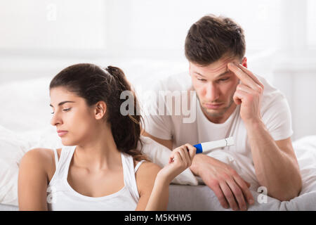 La donna che mostra la gravidanza positivo-test per suo marito preoccupati giacente sul letto Foto Stock