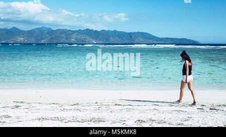 Una donna cammina attraverso le bianche sabbie della spiaggia di Le isole Gili, Bali Foto Stock