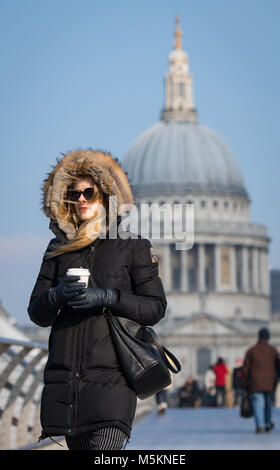 Una donna cammina attraverso il Millennium Bridge, nel centro di Londra, in condizioni ventose come il congelamento aria dalla Russia è di afferrare il Regno Unito in quanto è impostato in modo da essere il più freddo a fine febbraio in cinque anni. Foto Stock