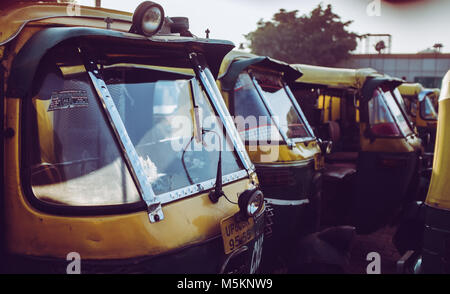 Una linea di giallo e verde-Tuk Tuk's schierate al di fuori della stazione di Agra in India. Foto Stock