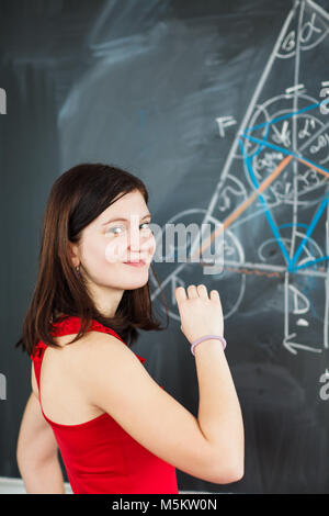 Ritratto di un bel giovane studente del collegio scrivere sulla lavagna durante una classe di matematica (toni di colore immagine) Foto Stock