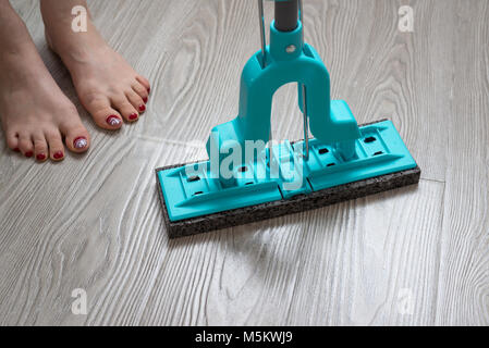 I piedi femminili e mop blu su sfondo di laminato Foto Stock