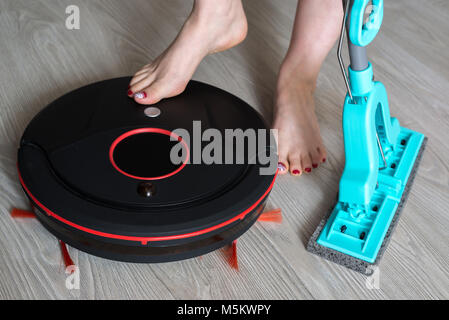 La donna comprende un manipolatore robotico aspirapolvere e detiene il mop Foto Stock