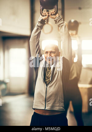 Montare uomo maturo in sportswear sorridente e oscillazione un peso durante una classe di allenamento in palestra Foto Stock