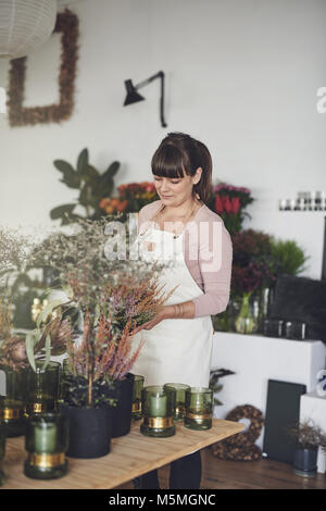 Sorridente giovane donna lavora da solo nel suo negozio di fiori di disporre vasi di fiori su una tabella di visualizzazione Foto Stock