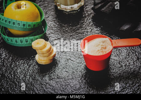 Proteine in polvere nel convogliatore e frutti sul tavolo di pietra Foto Stock
