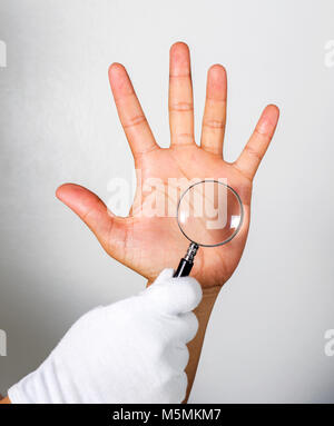 Guardando le linee sulla mano attraverso una lente di ingrandimento.su sfondo grigio. Foto Stock