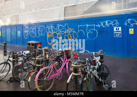 Biciclette concatenati per Rastrelliere per biciclette su un marciapiede davanti al sito in costruzione cartelloni coperto di graffiti tag nel centro di Cardiff Galles. Foto Stock