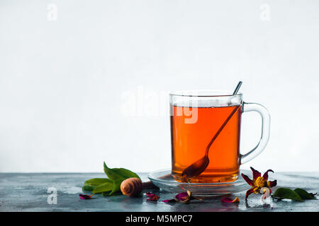 Il tè alle erbe in un bicchiere di vetro con un cucchiaio su uno sfondo luminoso con copia spazio. Alta molla chiave ancora il concetto di vita con foglie verdi, cucchiaio di miele e fiori secchi Foto Stock
