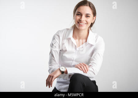 Ritratto di attracive giovane imprenditrice che indossa una camicia bianca e guardando la fotocamera mentre è seduto alla isolato sullo sfondo bianco. Foto Stock