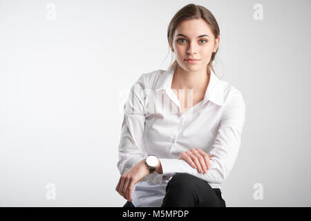 Ritratto di attracive giovane imprenditrice che indossa una camicia bianca e guardando la fotocamera mentre è seduto alla isolato sullo sfondo bianco. Foto Stock