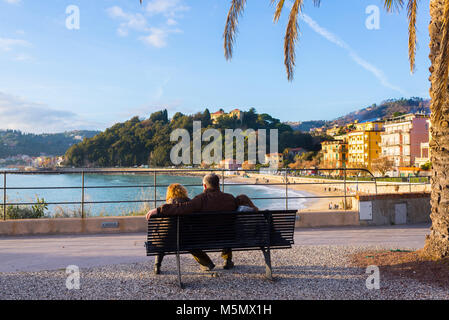 Famiglia di tre seduta su una panchina ammirando la vista sulla spiaggia della famosa località di mare città turistica di Lerici, Cinque Terre Liguria, Italia Foto Stock