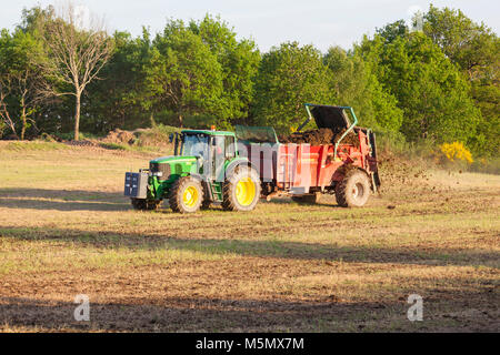 Agricoltore spargimento di concime organico, fertilizzante o concime su un pascolo della molla utilizzando un Degullaume muck spanditore e trattore John Deere Foto Stock