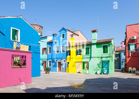 Isola di Burano, Venezia, Veneto, Italia. Case vivacemente colorate intorno a un campo o piazza dipinte in colori vivaci per guidare la casa di pescatori nella nebbia Foto Stock