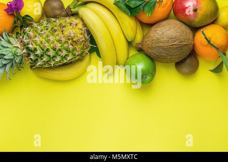 Varietà di differenti e tropicali Frutta estiva. Ananas Manghi Agrumi Noce di Cocco Arance Limoni Mele Kiwi banane disposto nel bordo superiore su giallo Foto Stock