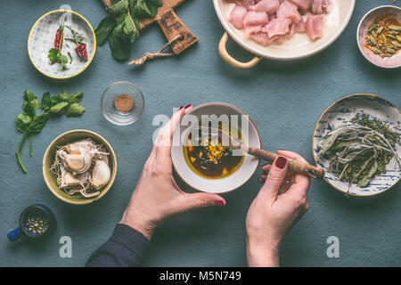 Mani femminili facendo macerare per carne di pollo pasto sul tavolo da cucina sfondo con ingredienti di bocce , vista dall'alto. Dieta mangiare cucina e salute Foto Stock