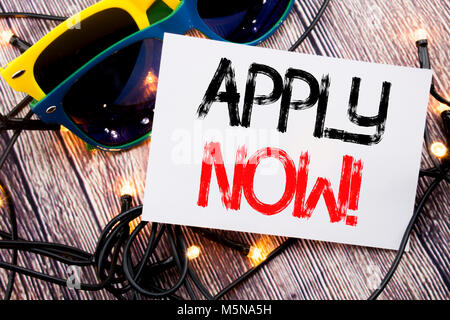 La scrittura di un testo che mostra Applica ora. Il concetto di business per il lavoro in affitto applicazione scritta sul legno vecchio sfondo di legno con occhiali da sole Foto Stock