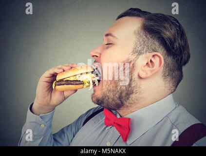 Profilo laterale di un uomo grasso di mangiare un hamburger succosa Foto Stock