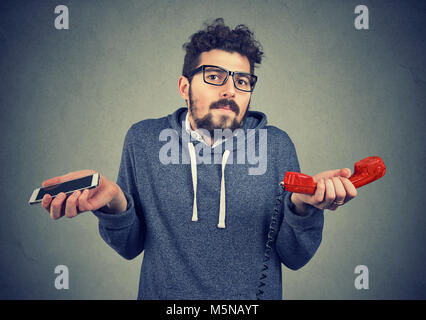 Giovane uomo informale guardando perplesso circa il vecchio stile contemporaneo e gadget. Foto Stock