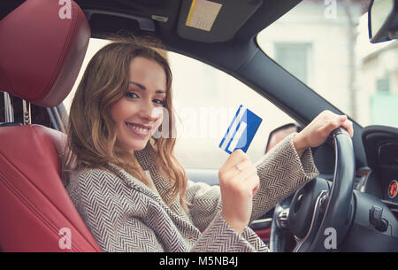 Felice giovane donna seduta dentro la sua nuova vettura che mostra carta di credito Foto Stock